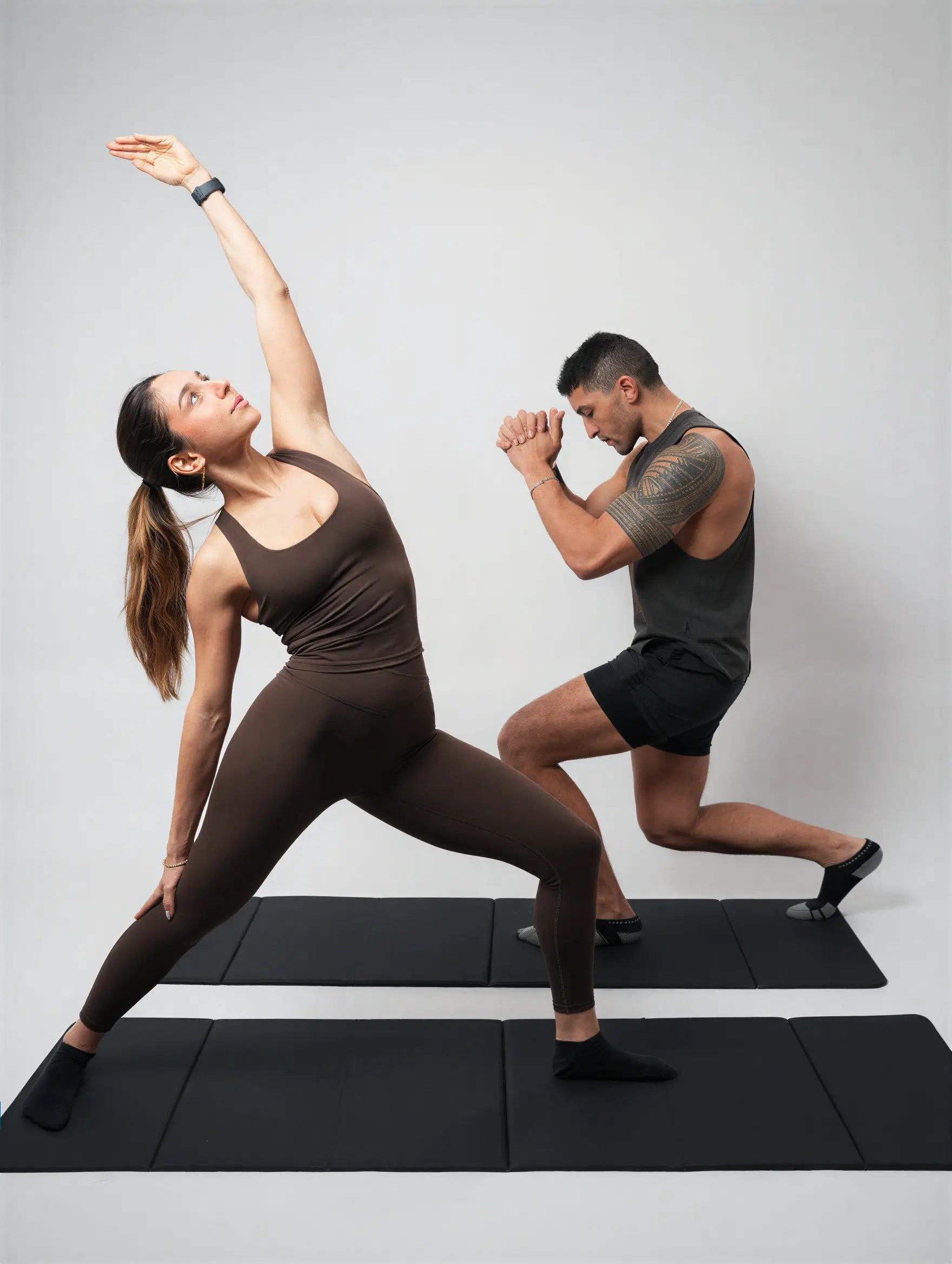 Two people in athletic wear performing yoga poses on a gray background