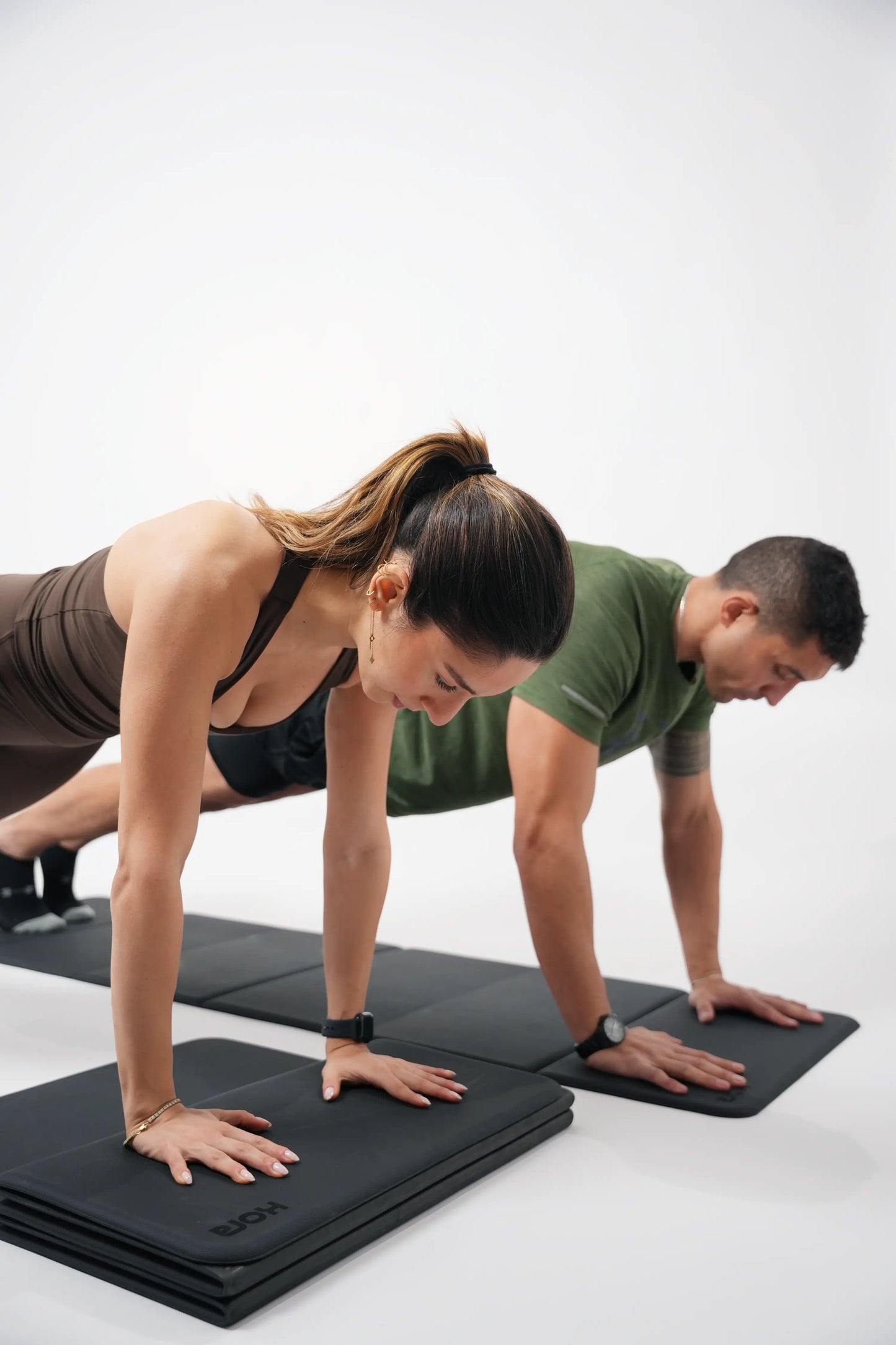 Two people in push-up positions on black mats with a white background