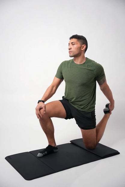 Man performing a yoga pose on a black mat against a white background