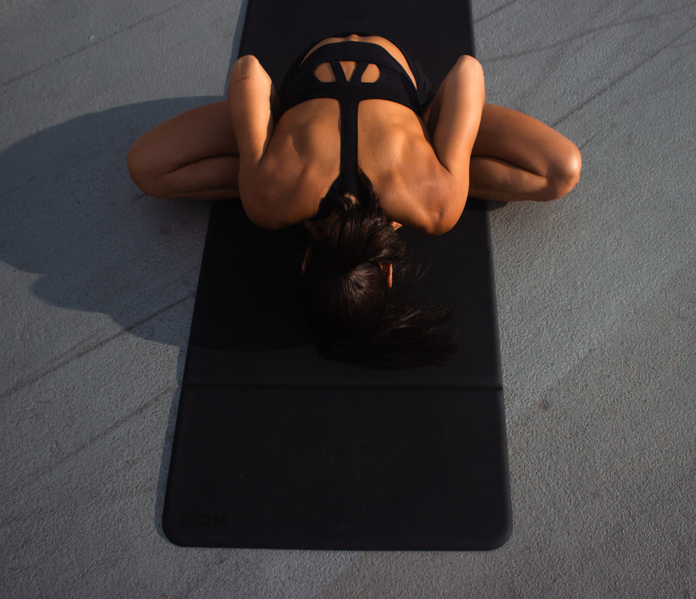 Person lying on a black yoga mat on a gray floor